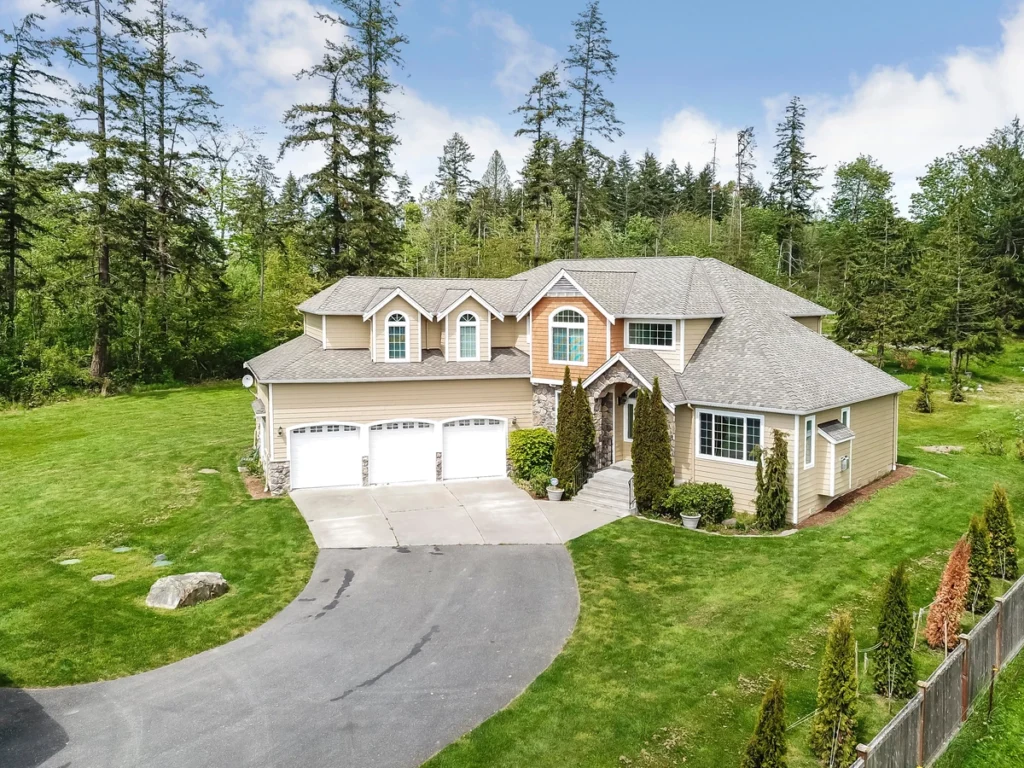 large luxury house with vinyl siding and gray asphalt shingle roof surrounded with trees